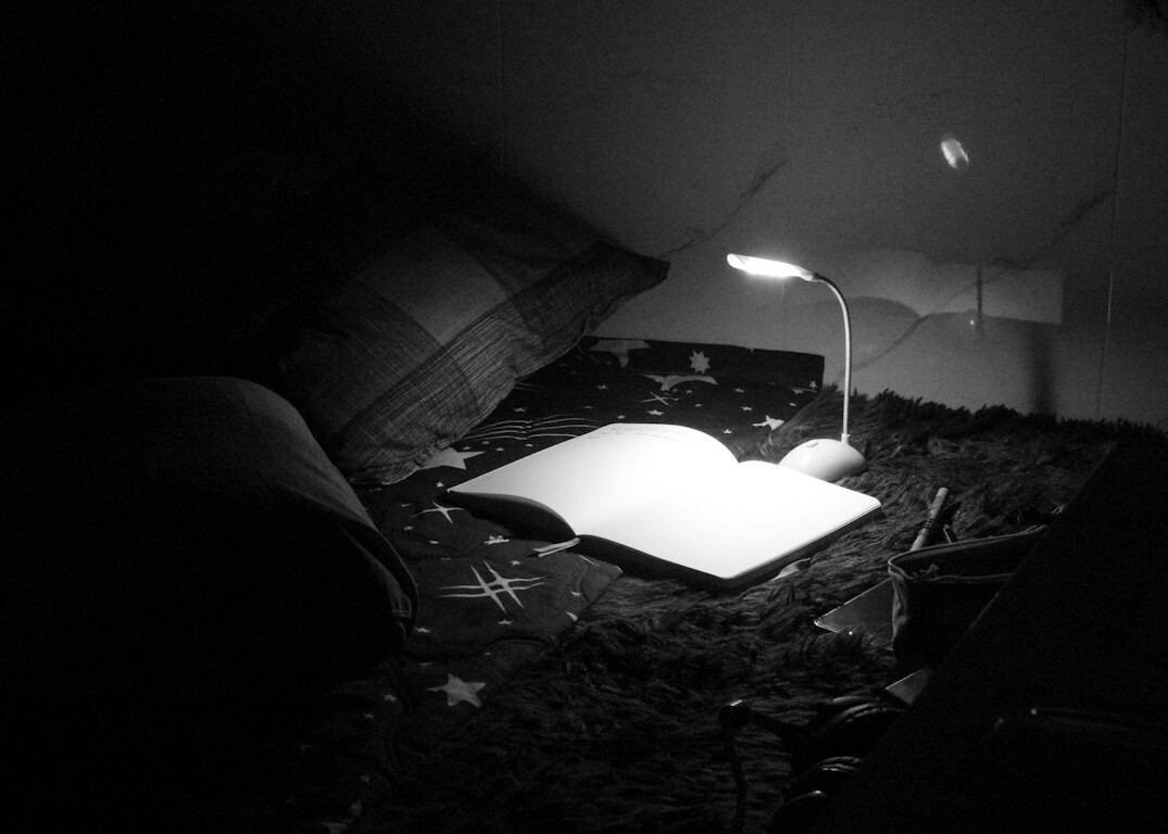 Open book on a table with a reading lamp and a magnifying glass at night
